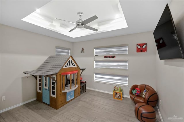 rec room with light wood-style floors, ceiling fan, baseboards, and a raised ceiling