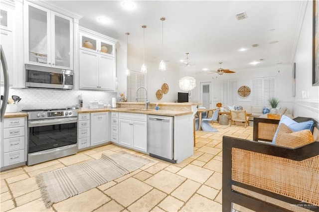 kitchen with sink, hanging light fixtures, stainless steel appliances, backsplash, and white cabinets