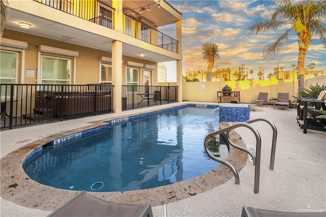 pool at dusk with pool water feature and a patio area