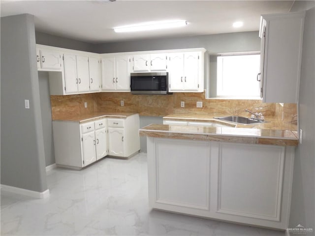 kitchen with backsplash, white cabinetry, kitchen peninsula, and sink