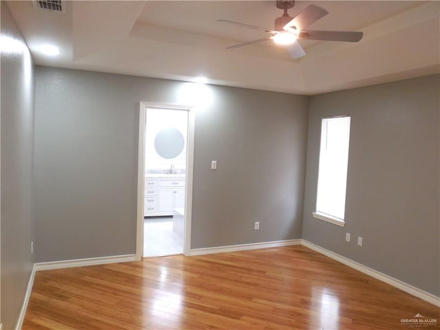 empty room featuring light wood-type flooring, a raised ceiling, ceiling fan, and sink