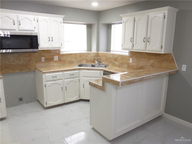 kitchen with backsplash, kitchen peninsula, white cabinetry, and sink