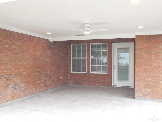 interior space featuring ceiling fan and brick wall