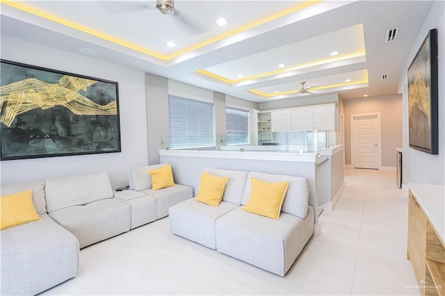 living room with a tray ceiling, ceiling fan, and light tile patterned floors