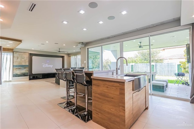 kitchen featuring sink, ceiling fan, light tile patterned floors, an island with sink, and a breakfast bar area