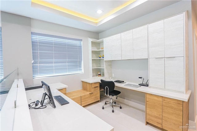 office with a raised ceiling, light tile patterned floors, and built in desk