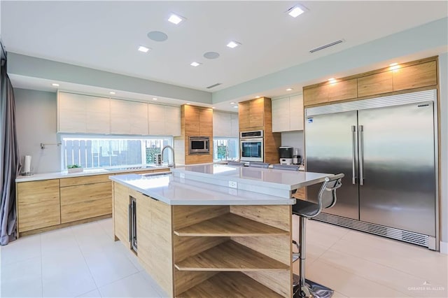 kitchen featuring a center island, sink, built in appliances, light tile patterned floors, and a breakfast bar area