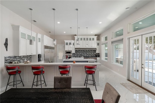 kitchen with pendant lighting, white cabinetry, stainless steel built in refrigerator, a breakfast bar area, and kitchen peninsula