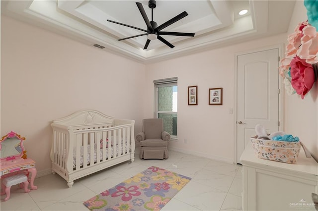 bedroom featuring a nursery area, ceiling fan, and a tray ceiling