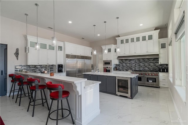 kitchen with a kitchen breakfast bar, premium appliances, white cabinets, decorative light fixtures, and beverage cooler