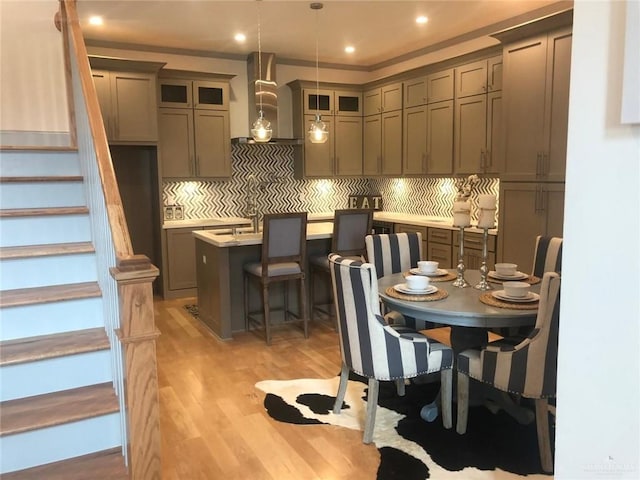 kitchen featuring wall chimney range hood, light hardwood / wood-style flooring, decorative light fixtures, a breakfast bar area, and a center island with sink