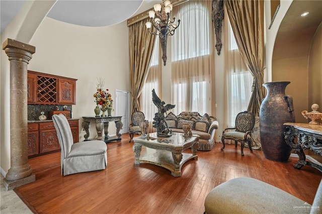 living room featuring arched walkways, a chandelier, a towering ceiling, and ornate columns
