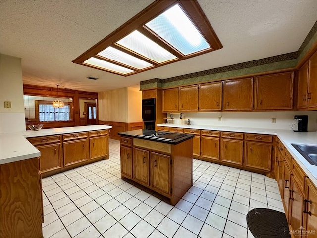 kitchen featuring light tile patterned floors, a textured ceiling, black appliances, brown cabinetry, and decorative light fixtures