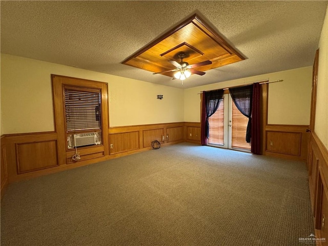 carpeted spare room with a textured ceiling, cooling unit, a ceiling fan, wainscoting, and a tray ceiling