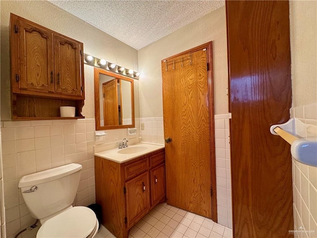 bathroom featuring a wainscoted wall, tile patterned floors, a textured ceiling, vanity, and tile walls