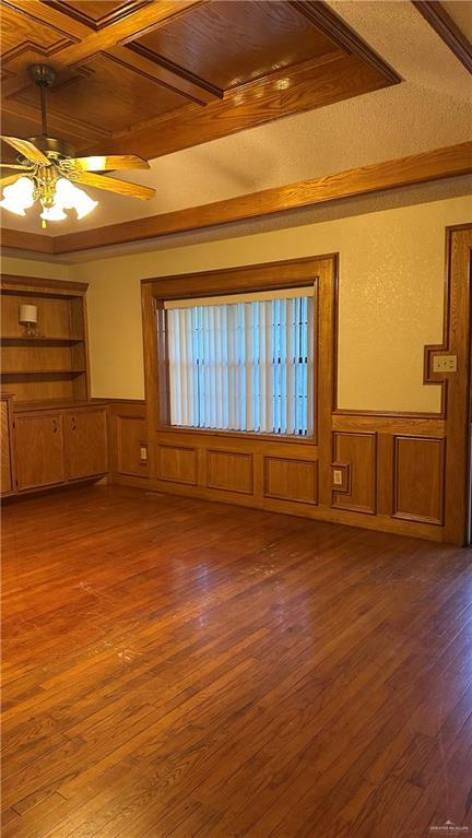 unfurnished living room with ceiling fan, beam ceiling, hardwood / wood-style floors, and wainscoting