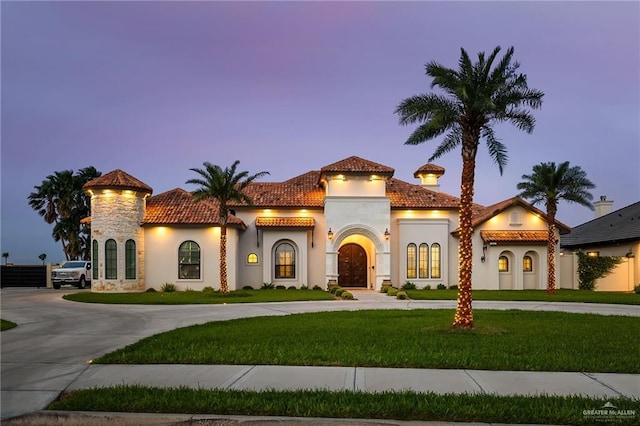 mediterranean / spanish-style home featuring stucco siding, a tiled roof, curved driveway, and a front lawn