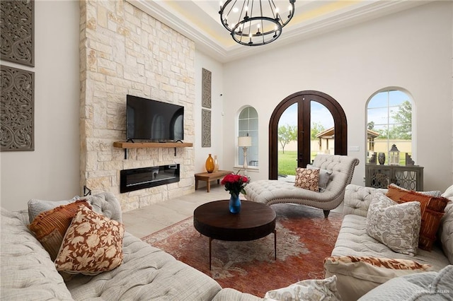 living area featuring crown molding, a towering ceiling, a stone fireplace, built in shelves, and a notable chandelier