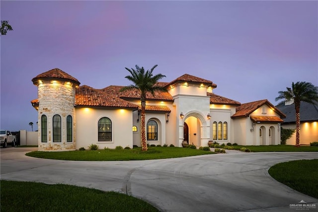 mediterranean / spanish-style house featuring stucco siding, a tiled roof, curved driveway, and a front lawn
