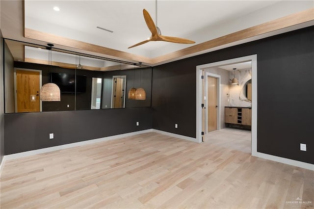 unfurnished room with ceiling fan, a raised ceiling, and light wood-type flooring