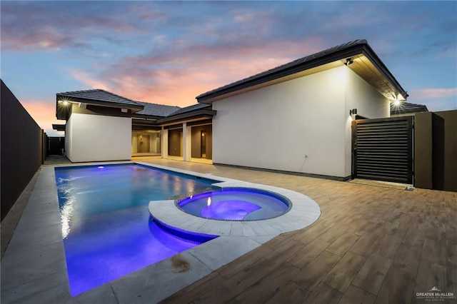 pool at dusk featuring an in ground hot tub