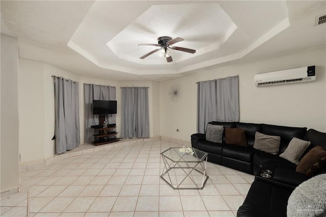 living area with a wall unit AC, light tile patterned floors, a ceiling fan, baseboards, and a tray ceiling