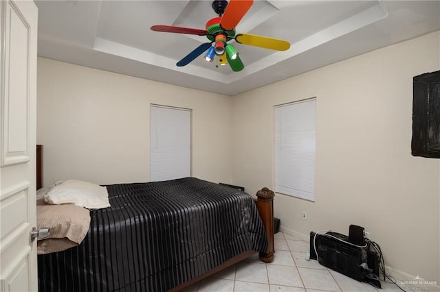 bedroom featuring ceiling fan, light tile patterned flooring, and a tray ceiling