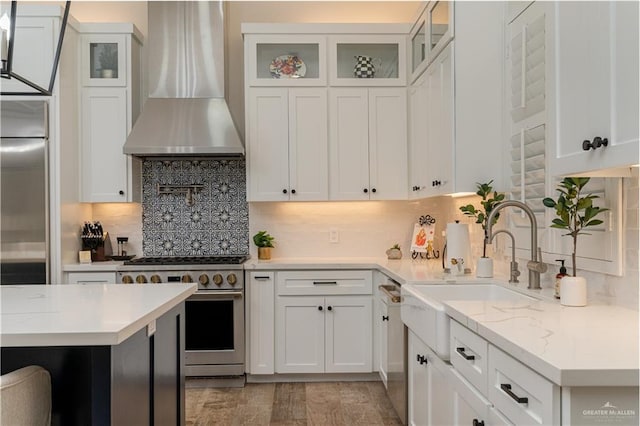 kitchen featuring stainless steel appliances, wall chimney range hood, white cabinets, and light stone counters