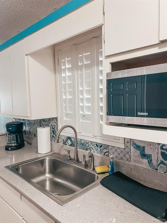 kitchen featuring white cabinets, a textured ceiling, backsplash, and sink