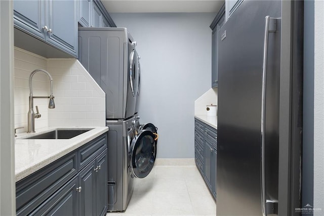 clothes washing area featuring cabinets, light tile patterned floors, stacked washer and clothes dryer, and sink