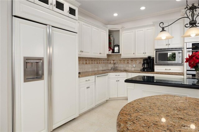 kitchen with crown molding, built in appliances, decorative light fixtures, light stone counters, and white cabinetry