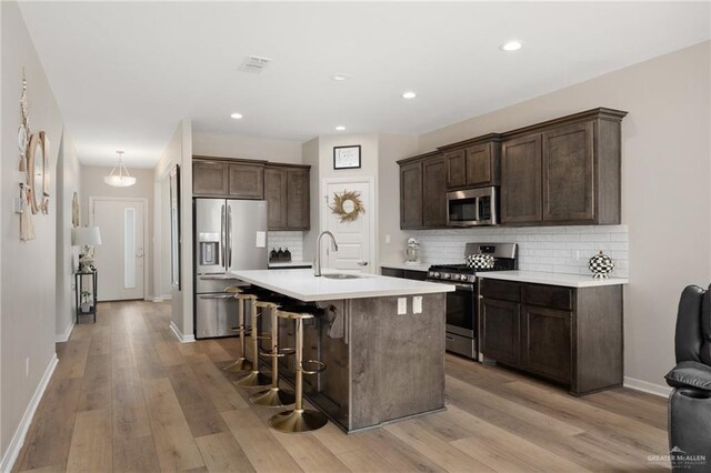 kitchen featuring sink, light hardwood / wood-style flooring, appliances with stainless steel finishes, tasteful backsplash, and a breakfast bar area