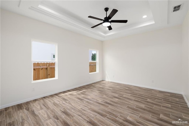 empty room featuring hardwood / wood-style floors, ceiling fan, and a tray ceiling