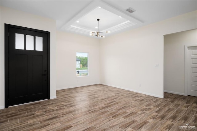 foyer entrance featuring a tray ceiling, wood-type flooring, and a notable chandelier