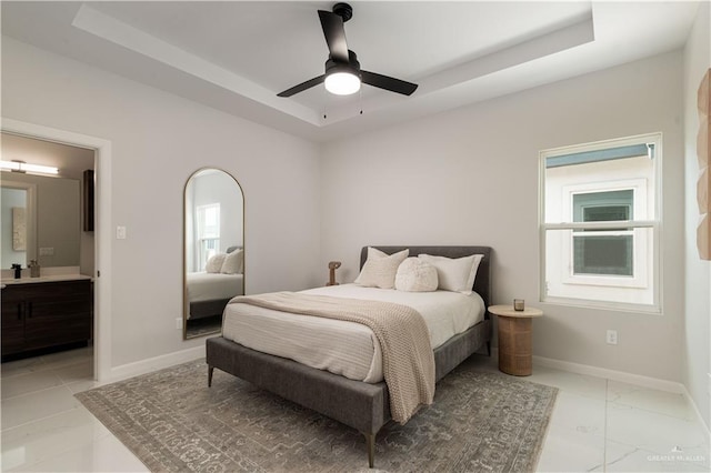 bedroom featuring ceiling fan, connected bathroom, and a tray ceiling