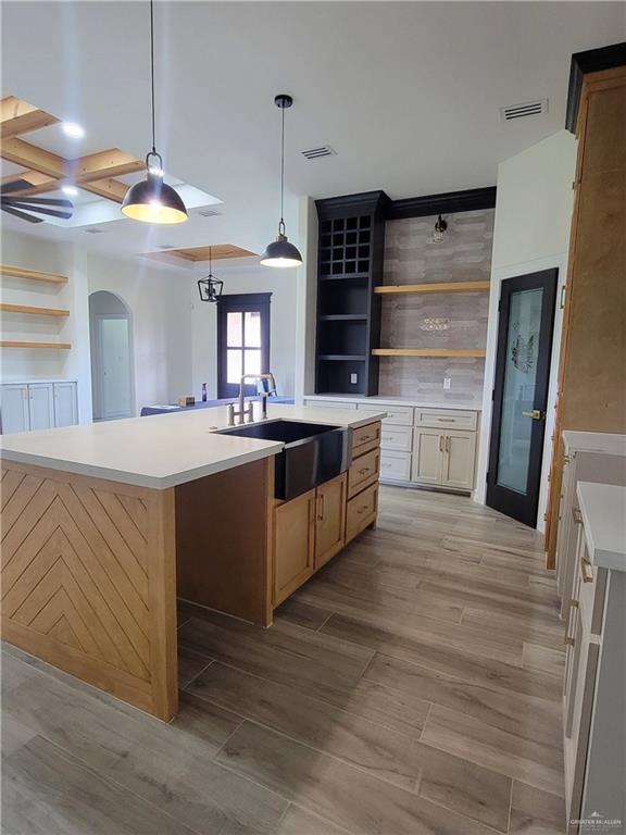 kitchen with a large island with sink, light hardwood / wood-style floors, pendant lighting, and sink