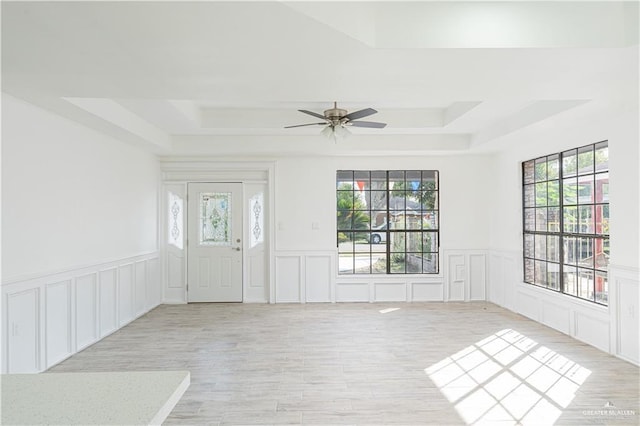 entryway with light wood-type flooring, a tray ceiling, and ceiling fan