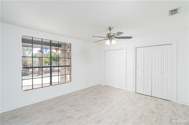 unfurnished bedroom with ceiling fan, light wood-type flooring, and multiple closets