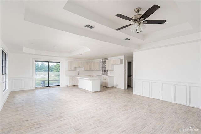 unfurnished living room featuring a tray ceiling, ceiling fan, and light hardwood / wood-style flooring