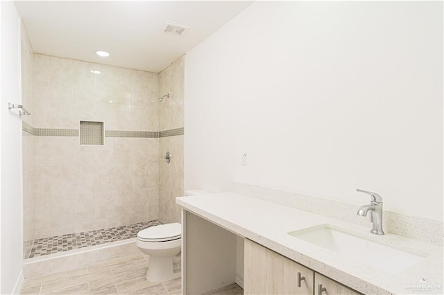 bathroom featuring a tile shower, vanity, and toilet