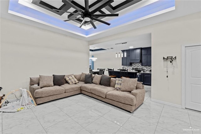 living room featuring marble finish floor, baseboards, a tray ceiling, and a ceiling fan