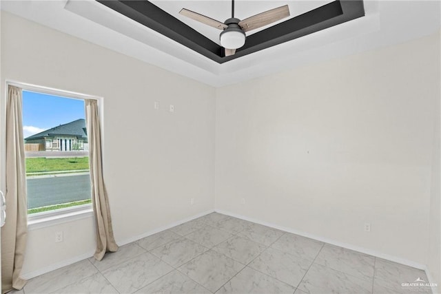 empty room featuring a raised ceiling, plenty of natural light, and marble finish floor