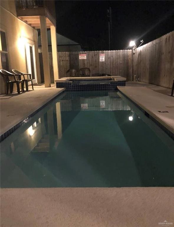 pool at twilight with a jacuzzi and a patio