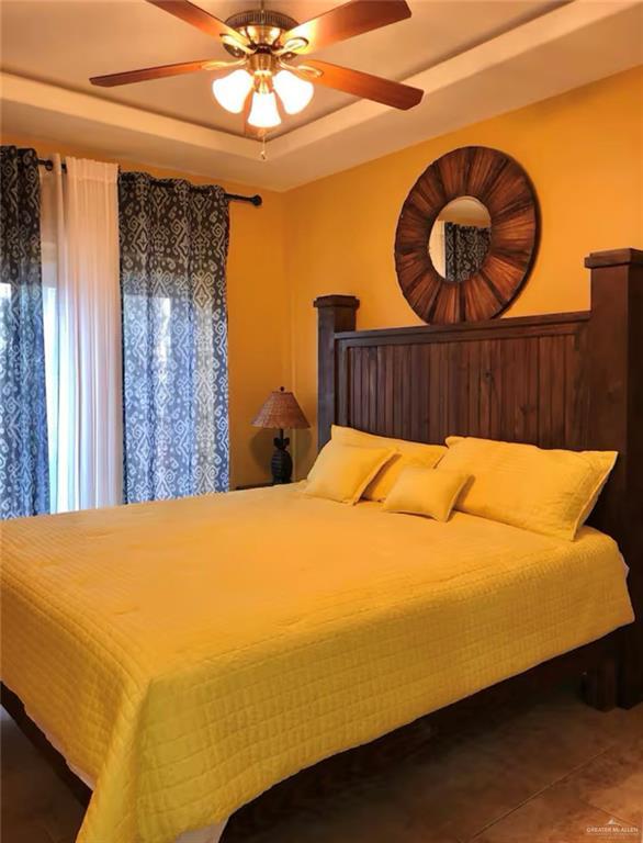 bedroom featuring a tray ceiling, ceiling fan, and wooden walls