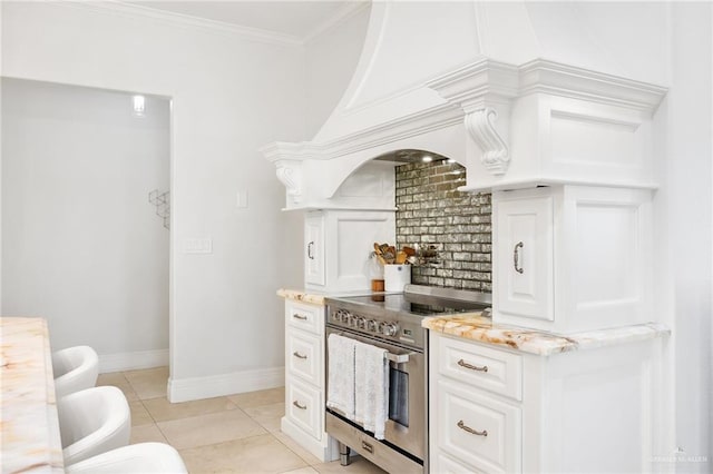 kitchen featuring light stone counters, crown molding, light tile patterned floors, stainless steel stove, and white cabinetry