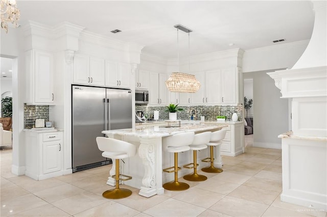 kitchen featuring white cabinets, hanging light fixtures, decorative backsplash, an island with sink, and appliances with stainless steel finishes