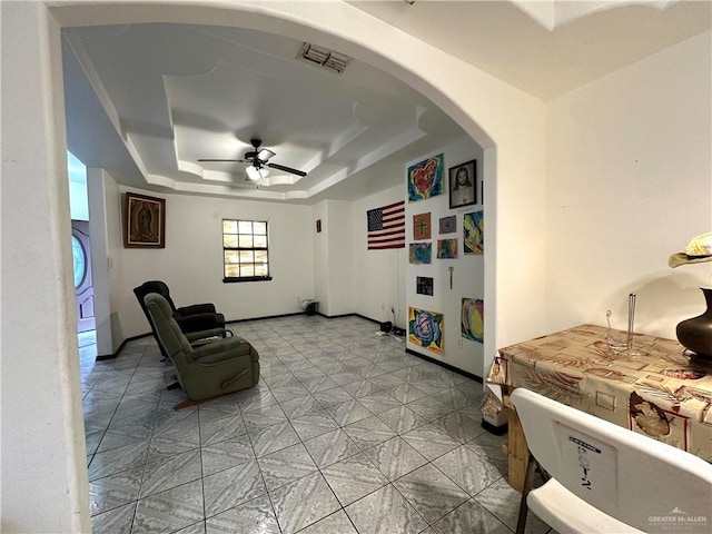 living area featuring ceiling fan and a raised ceiling