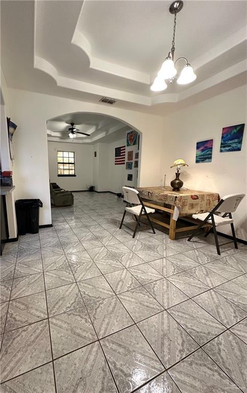 unfurnished dining area with ceiling fan with notable chandelier and a raised ceiling