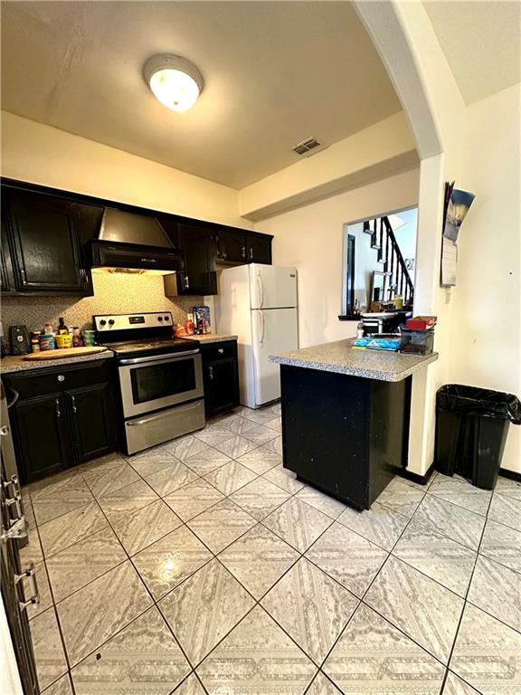 kitchen featuring stainless steel electric stove, wall chimney exhaust hood, and white fridge