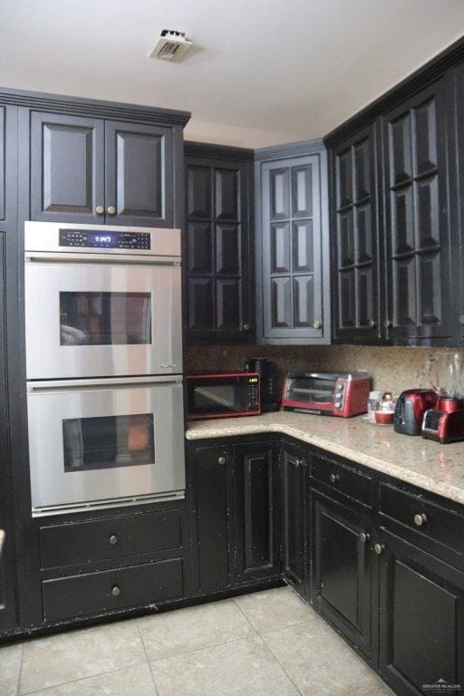 kitchen with light stone counters, double oven, and light tile patterned floors